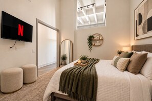 Une chambre à coucher avec un lit, des tables de chevet, une télévision, un miroir et une fenêtre.