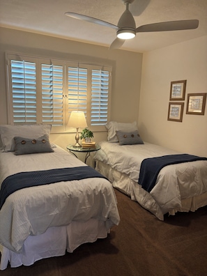A bedroom with two beds, a ceiling fan, a lamp, and a small table with a clock and books. - Amazing Chaparral Country Club Updated Town Home on 6th Tee Box. (Palm Desert)