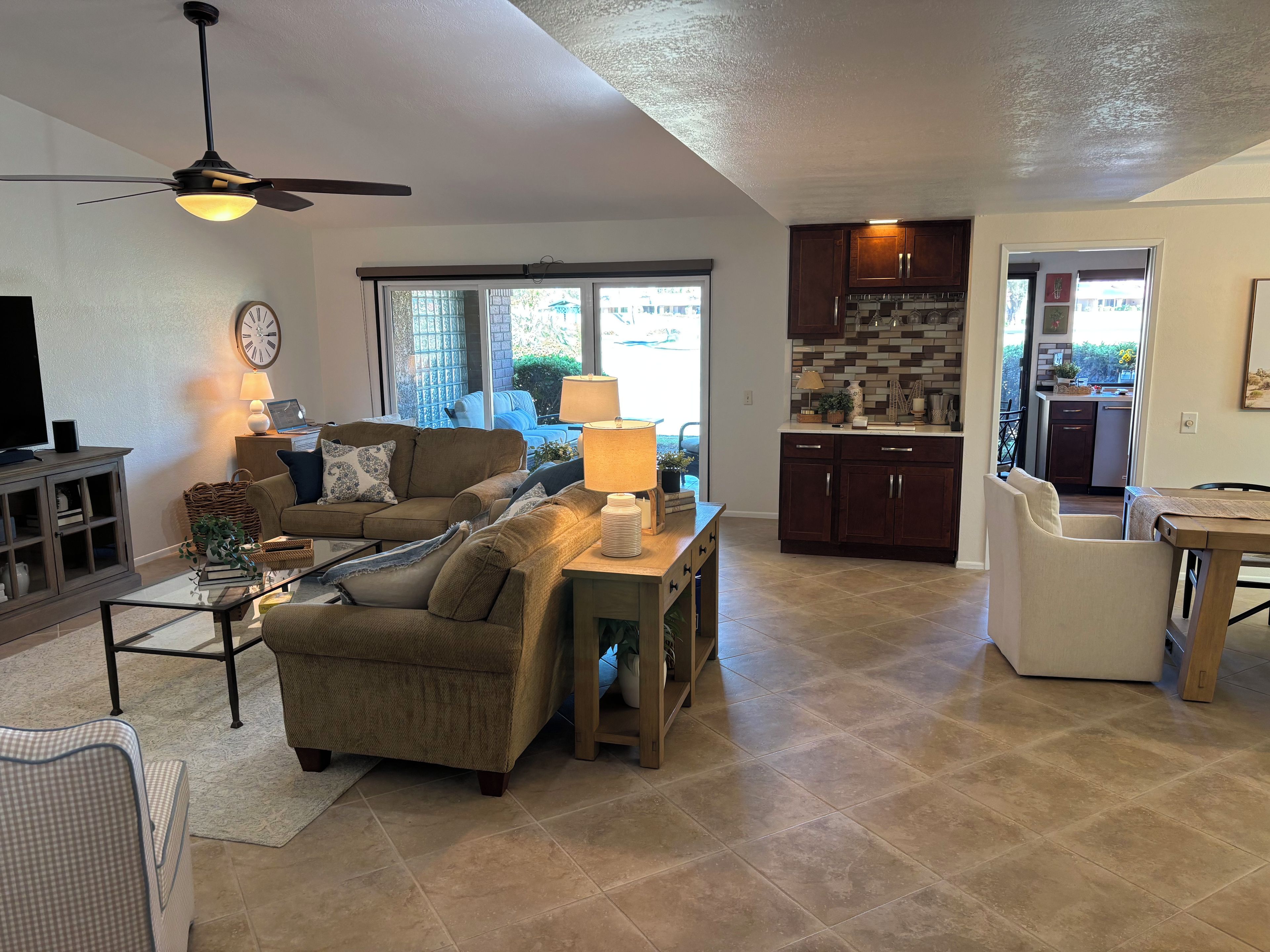 A living room with a sofa, coffee table, and a television. There is a kitchen area with cabinets and a window.