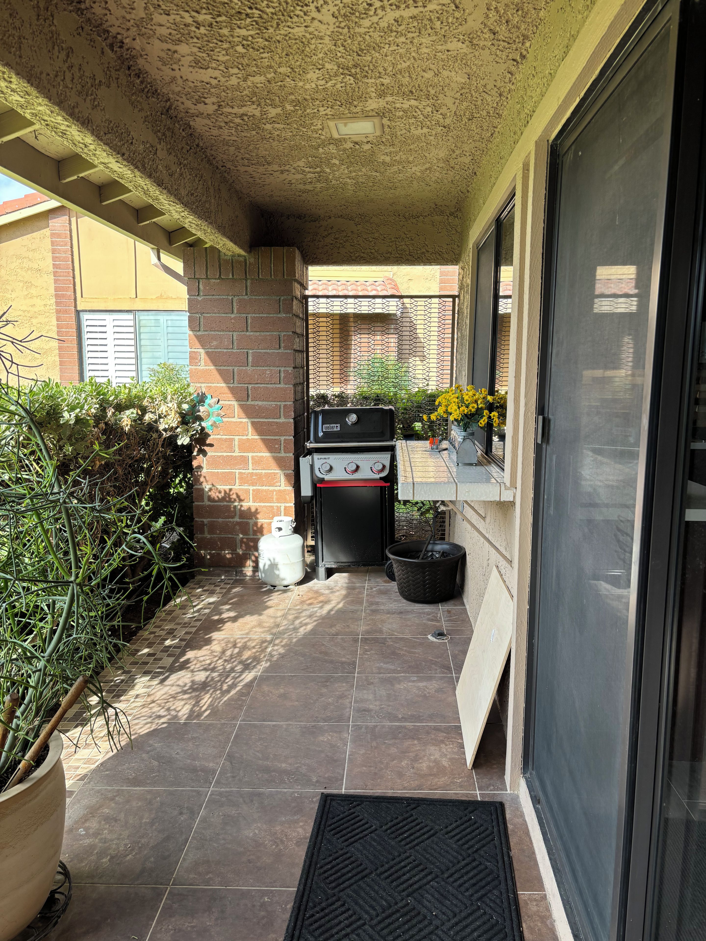 A covered outdoor area with a barbecue grill, a gas cylinder, and potted plants.