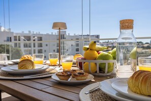 A breakfast table with croissants, pastries, fruit, and orange juice on a terrace with a city view. - Two-Bedroom Apartment with Pool and Balcony in Albufeira, Algarve (Albufeira)