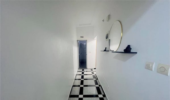Un pasillo con piso a cuadros, una puerta al final y un espejo con un pequeño estante.