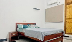 A single bed with a wooden frame, a bedside table, and a wall-mounted air conditioning unit. - Residence Leboncoin 1 (abidjan)