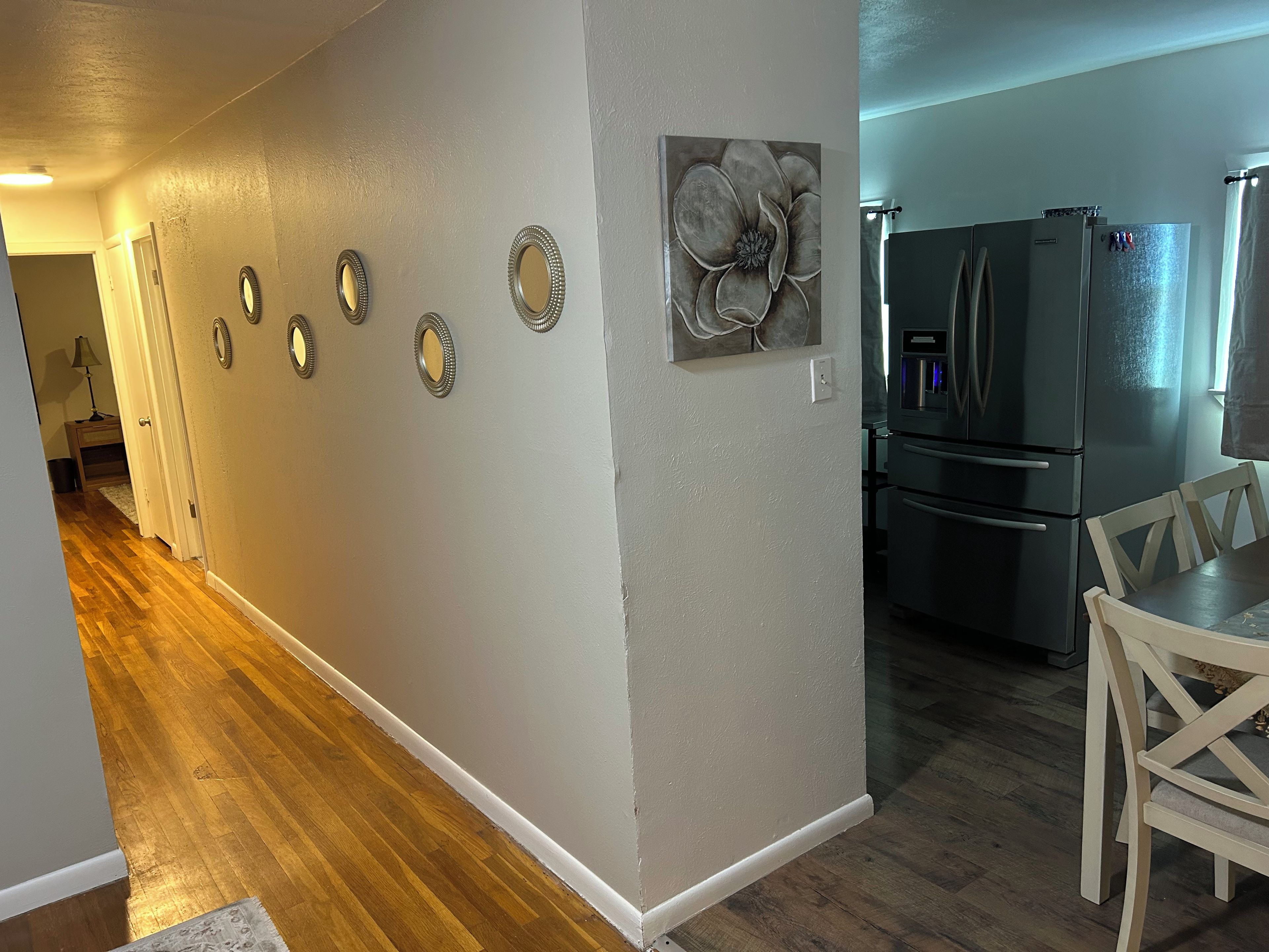 Um corredor com piso de madeira, uma sala de jantar com mesa e cadeiras, e uma cozinha com geladeira.