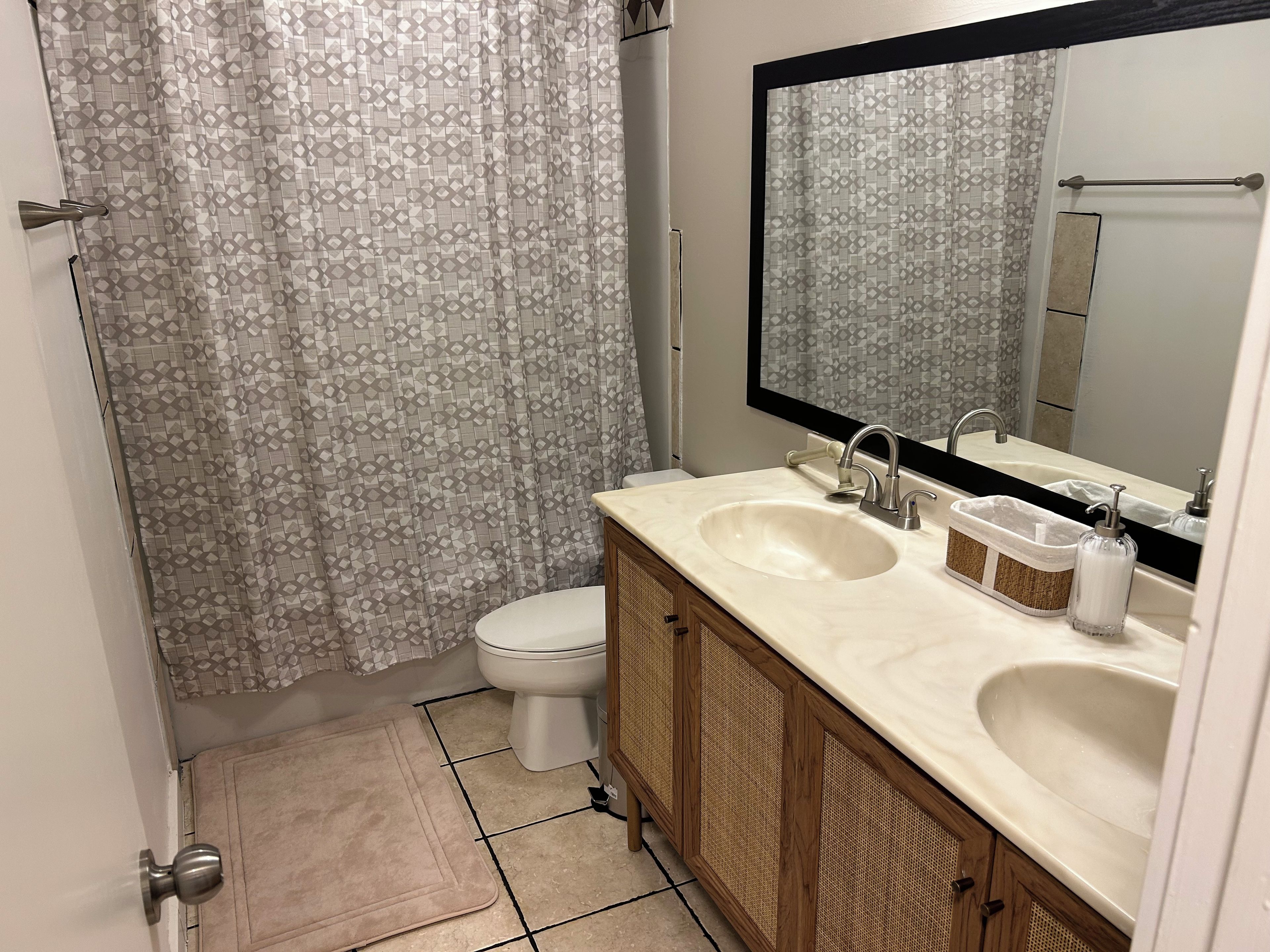 A bathroom with a toilet, two sinks, a mirror, and a shower curtain.