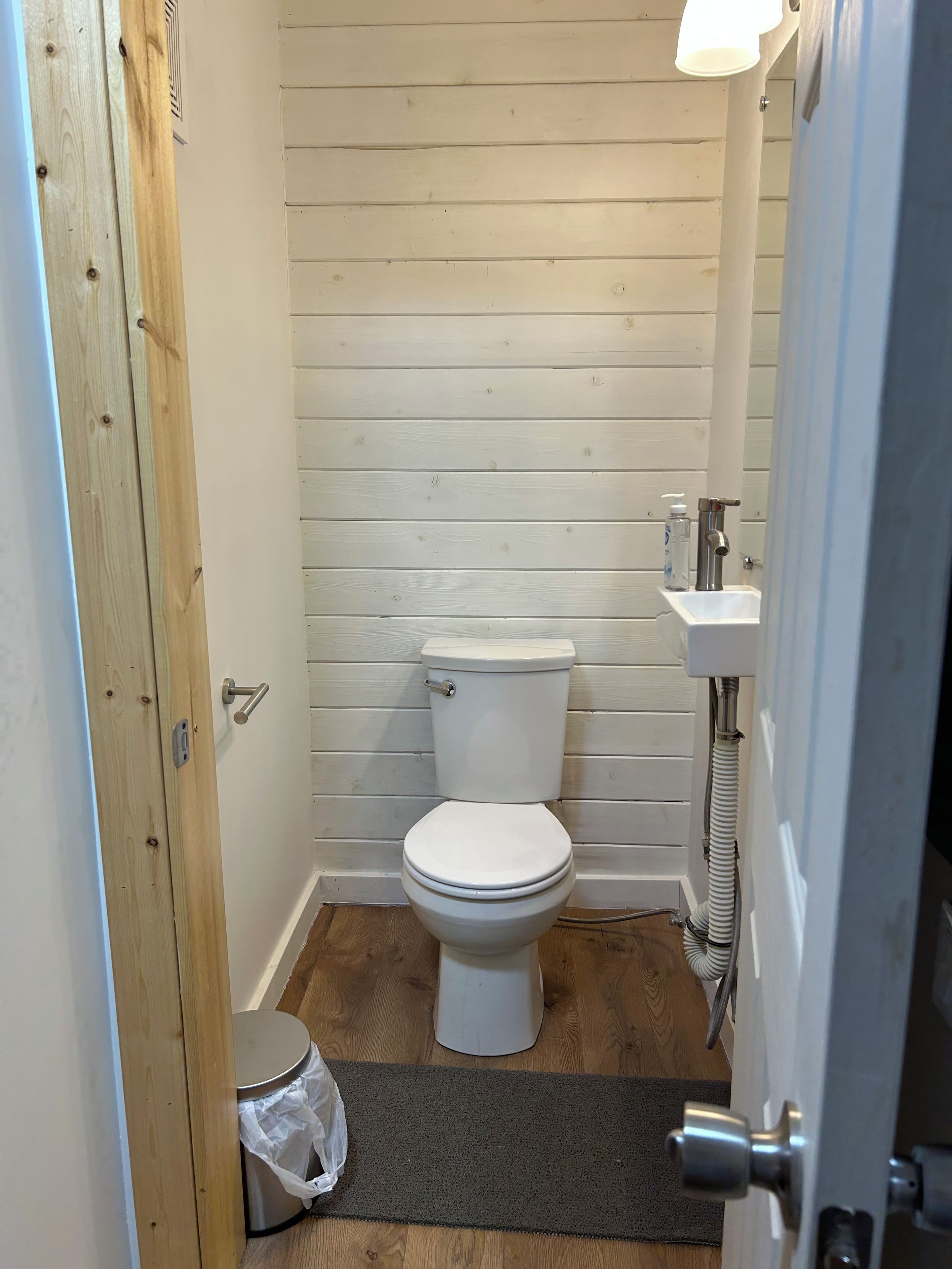 A small, narrow bathroom with a white toilet, a wooden door, and a white sink.