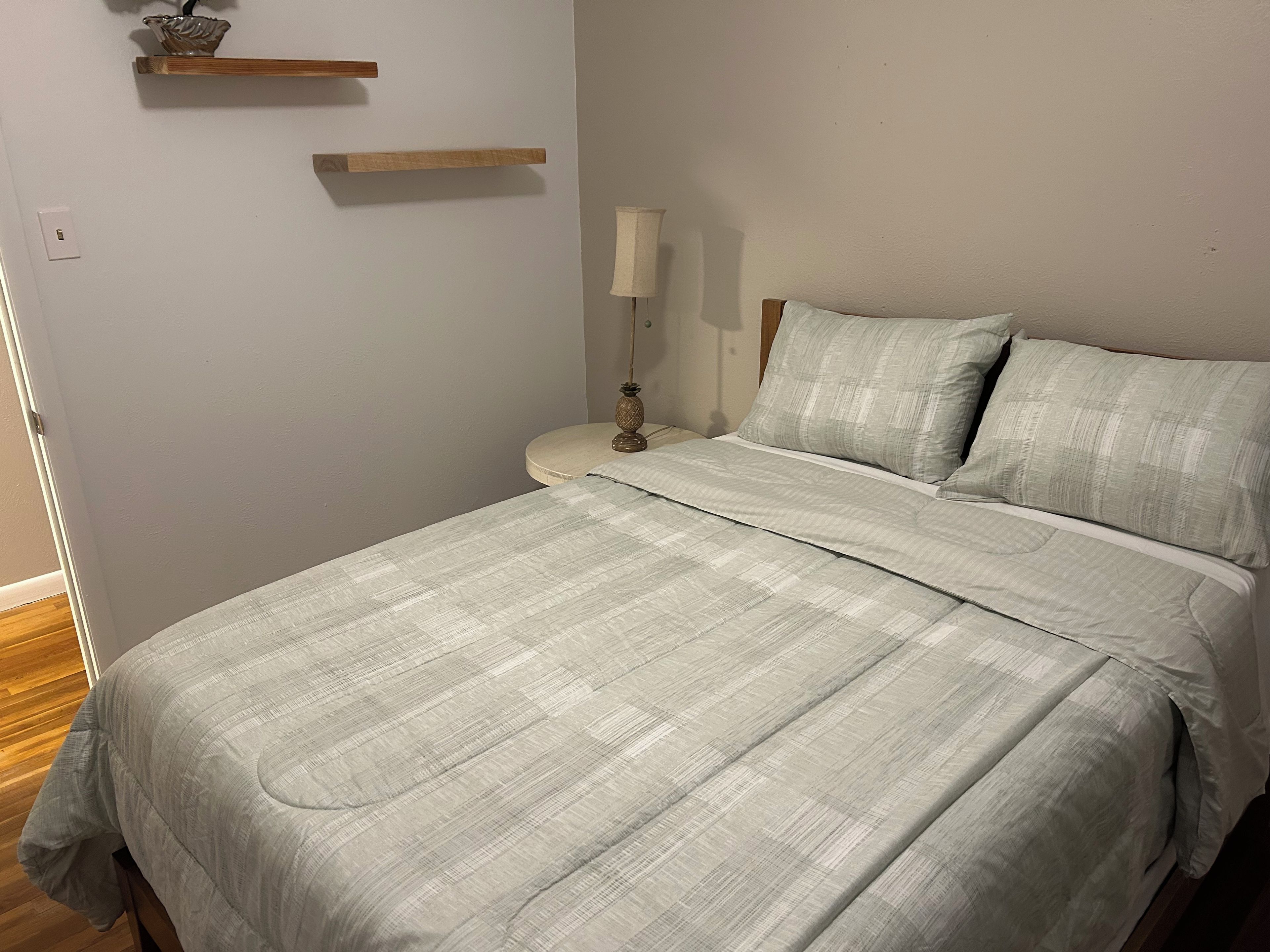 A bedroom with a bed, bedside table, lamp, and two wooden shelves.
