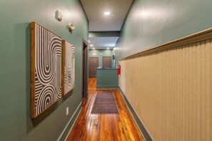 Un pasillo con suelo de madera, paredes verdes y dos puertas que dan a una habitación.