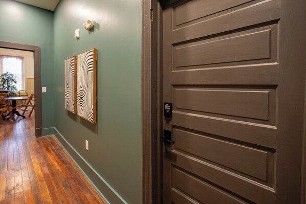A hallway with a wooden floor, a brown door, and two wall-mounted artworks.