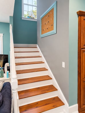 A staircase with wooden steps and white railings, a corkboard on the wall, and a window with a sailboat model. - Relaxing 2-bedroom pool house - Bedford, IN. Easy drive for IU Football (Bedford)