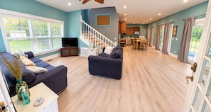 A spacious living room with a staircase leading to a kitchen, large windows, and a dining area. - Relaxing 2-bedroom pool house - Bedford, IN. Easy drive for IU Football (Bedford)