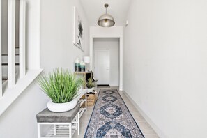 A hallway with a white bench, a potted plant, a rug, and a door at the end. - #1 Anaheim Gem-Disney-Stadium-Honda Center-Pool-Spa-BBQ-Park (Anaheim)