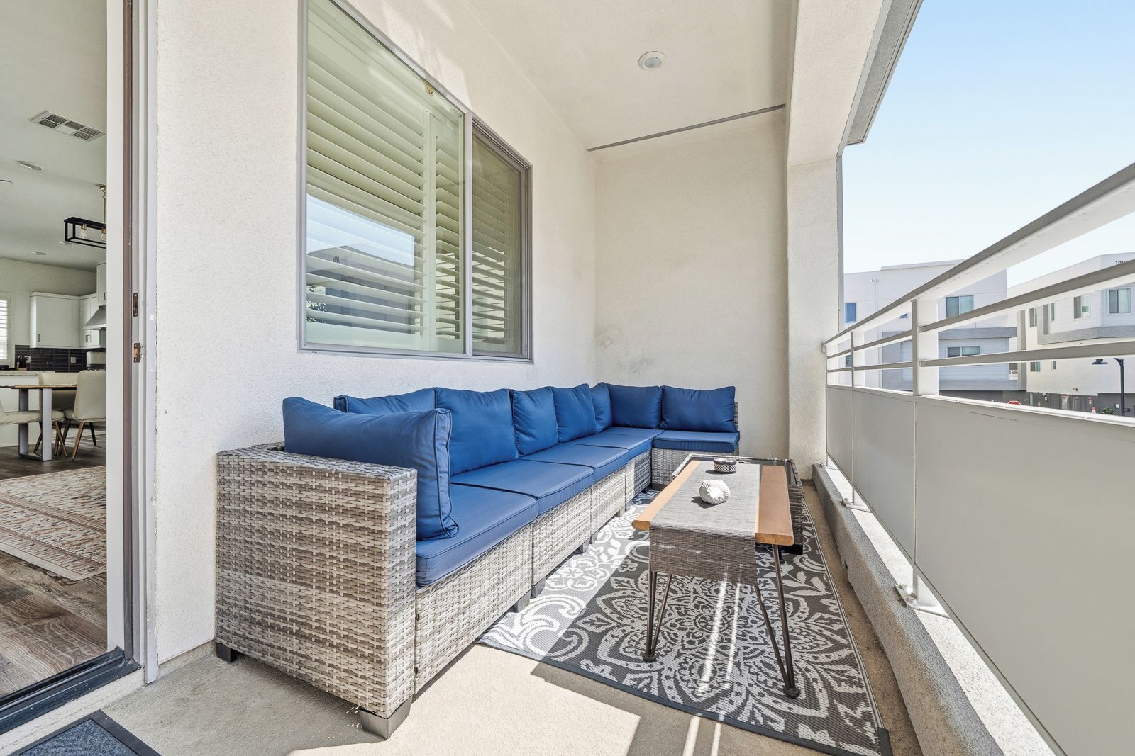 A balcony with a wicker sofa, a small table, and a patterned rug.