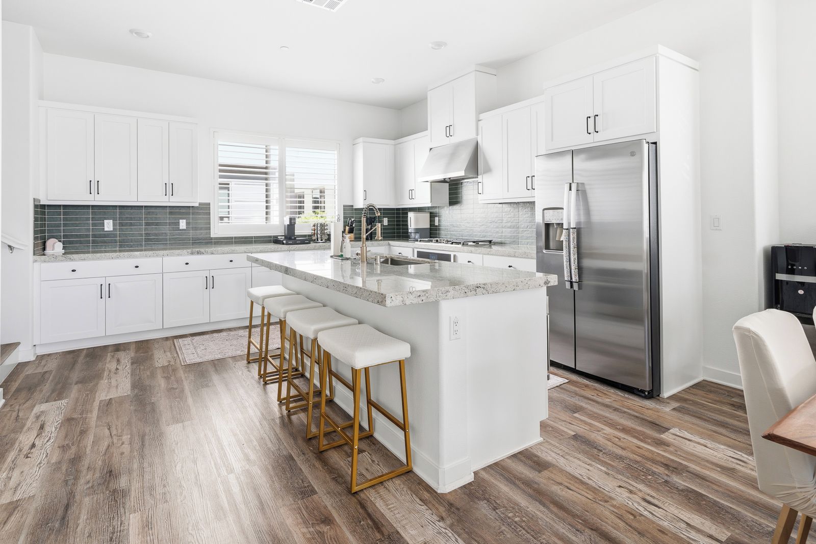 A modern kitchen with white cabinetry, a stainless steel refrigerator, and a central island with bar stools.