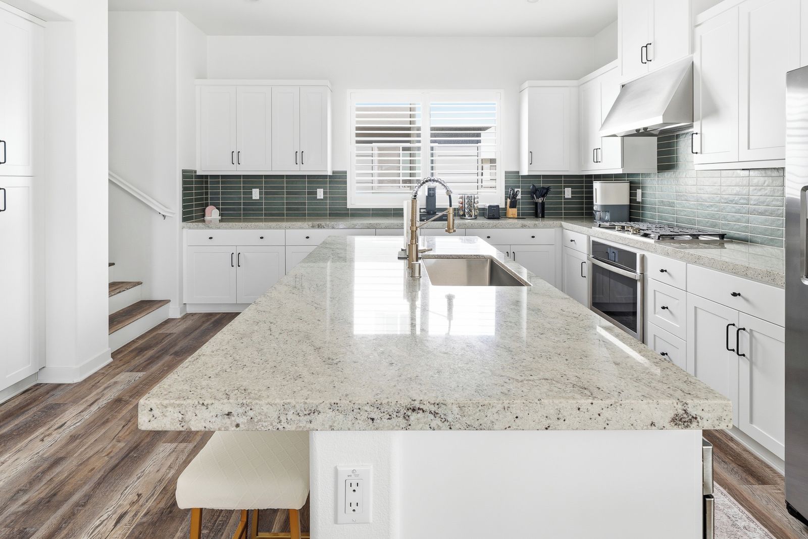 A modern kitchen with white cabinetry, a granite countertop, and a stainless steel range hood.