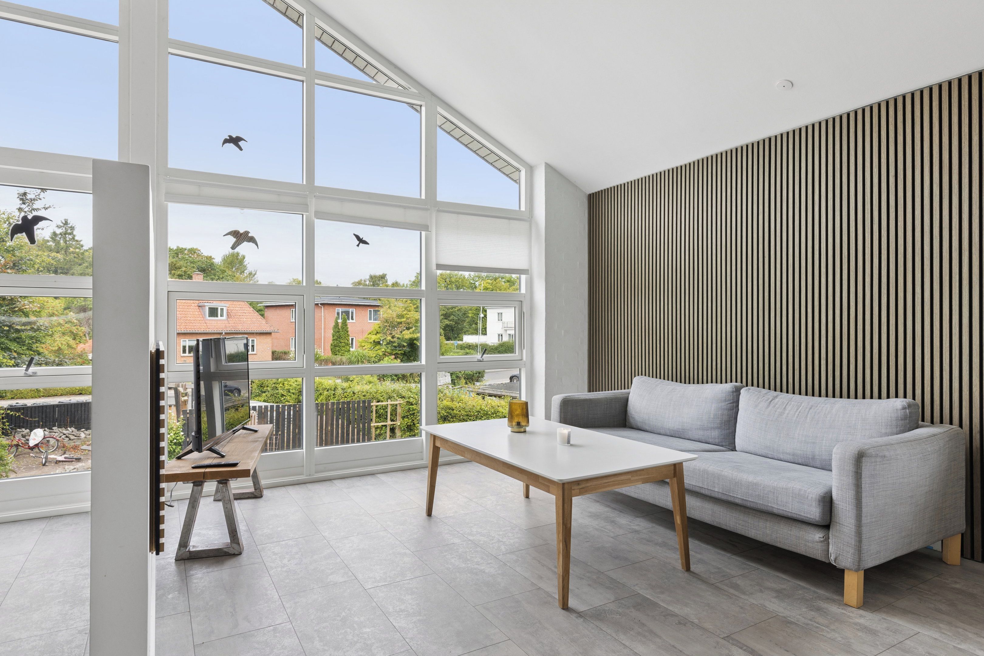 Una sala de estar moderna con un sofá gris, una mesa de centro de madera y un amplio ventanal con vistas al exterior.