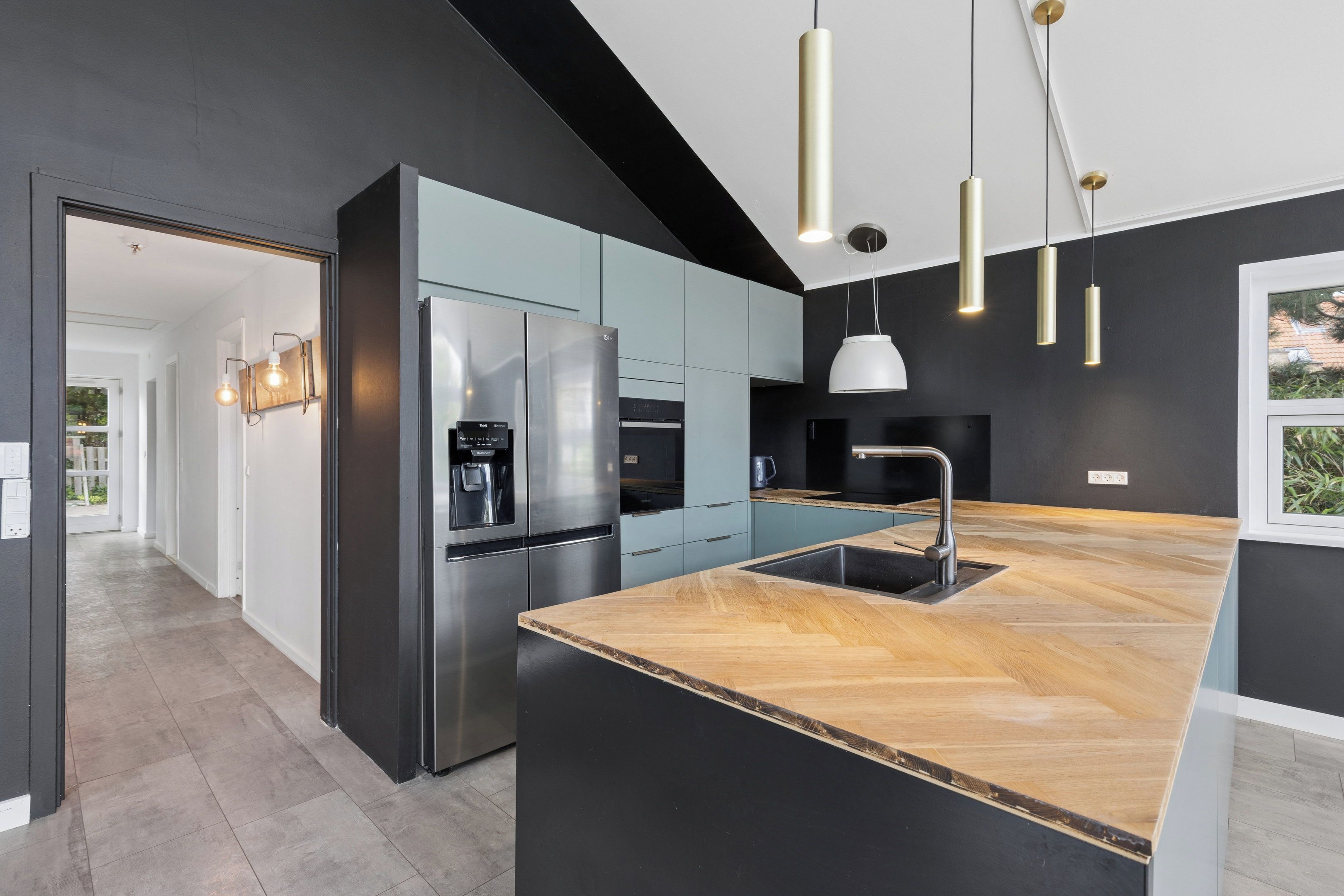 Une cuisine moderne dotée d’un grand îlot central, d’appareils électroménagers en acier inoxydable et de luminaires suspendus.