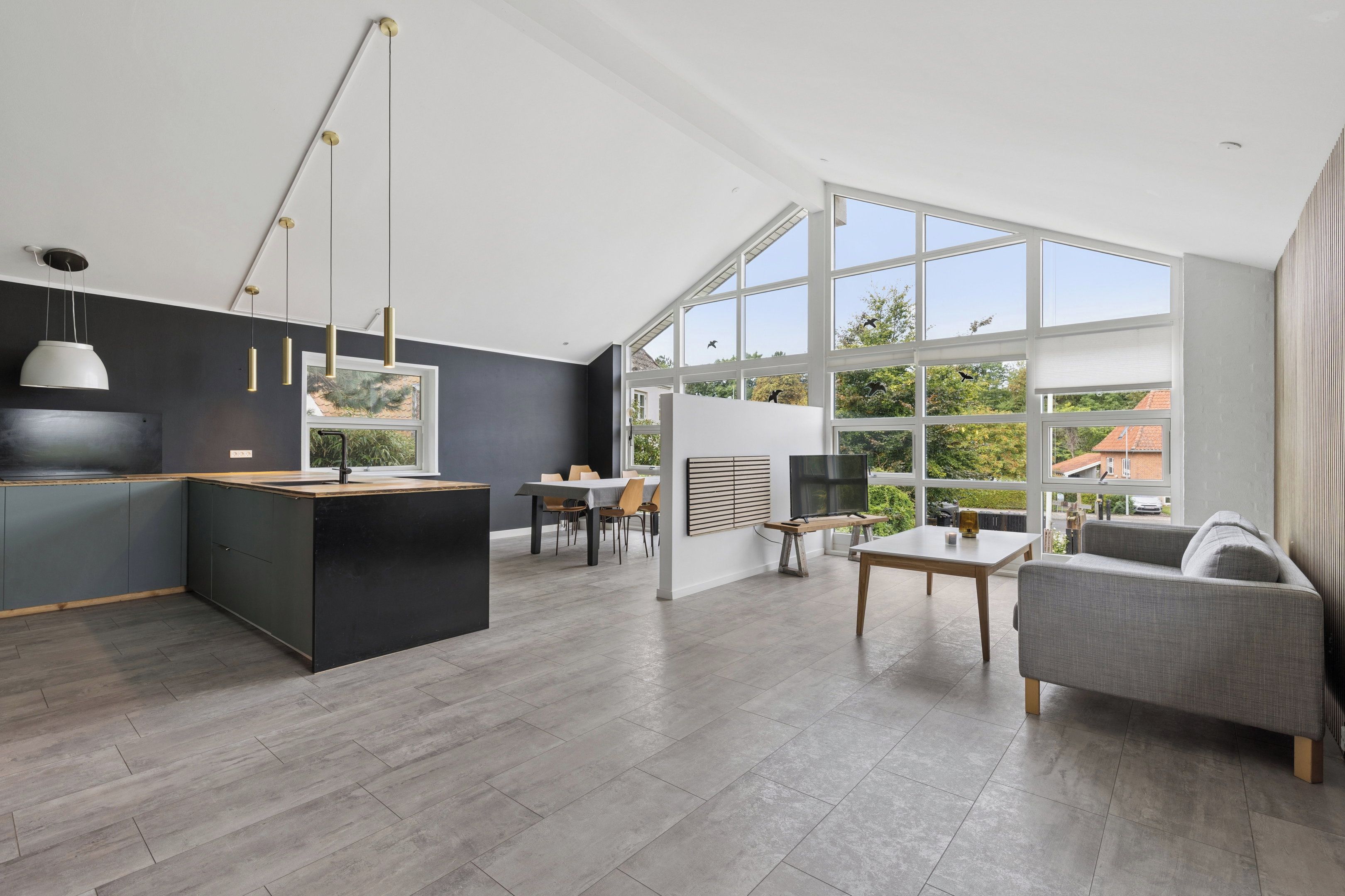 A modern kitchen with a central island, a dining area with a table and chairs, and a living area with a sofa and a TV.