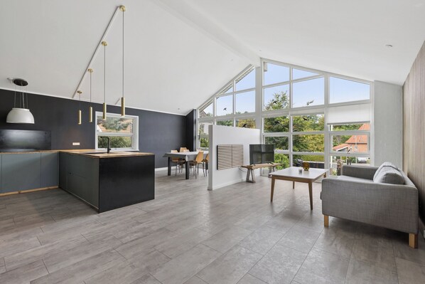 A modern kitchen with a central island, a dining area with a table and chairs, and a living area with a sofa and a TV.