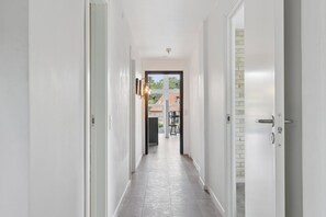 A hallway with white walls, a tiled floor, and a door leading to a balcony with a view of buildings.