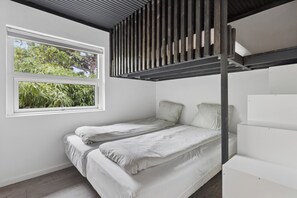 A bunk bed with a window overlooking greenery, a white wall, and a slanted ceiling.