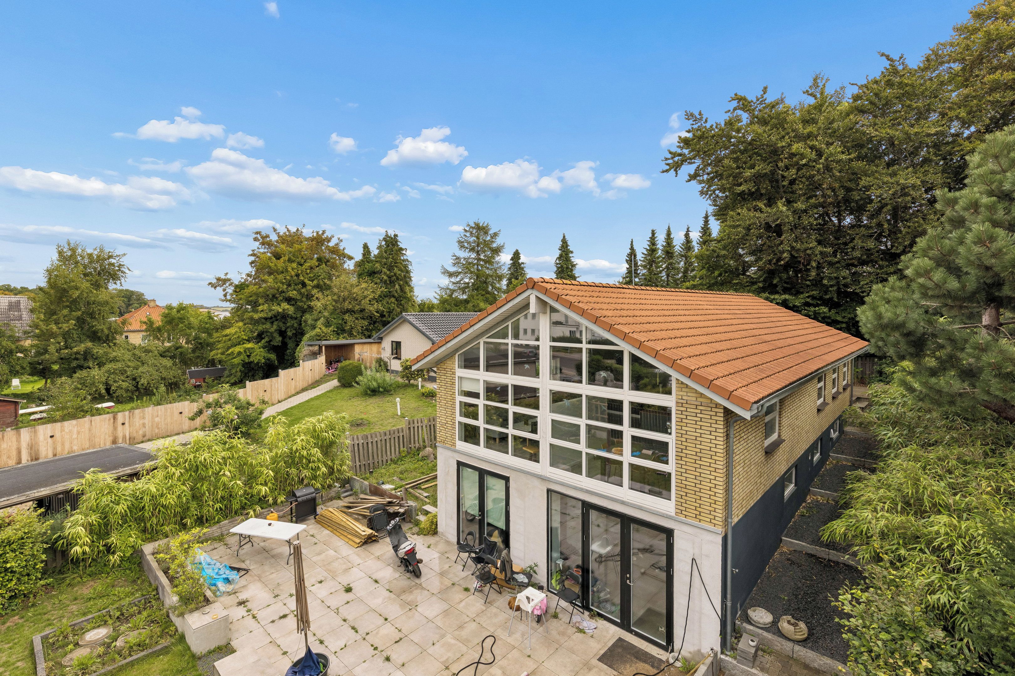 A residential property with a large glass window facade, a sloped roof, and a backyard with a patio area.