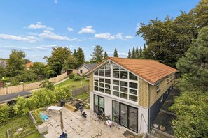 A residential property with a large glass window facade, a sloped roof, and a backyard with a patio area.