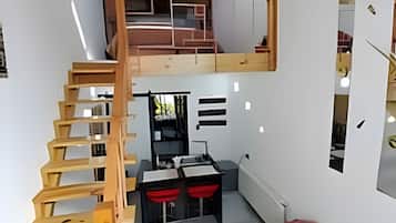 A compact room with a wooden staircase leading to a loft area, a kitchenette, and a seating area with a sofa.