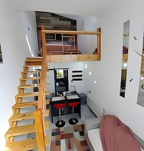 A compact room with a wooden staircase leading to a loft area, a kitchenette, and a seating area with a sofa. - Okeyloft 4 Coyhaique (Coyhaique)