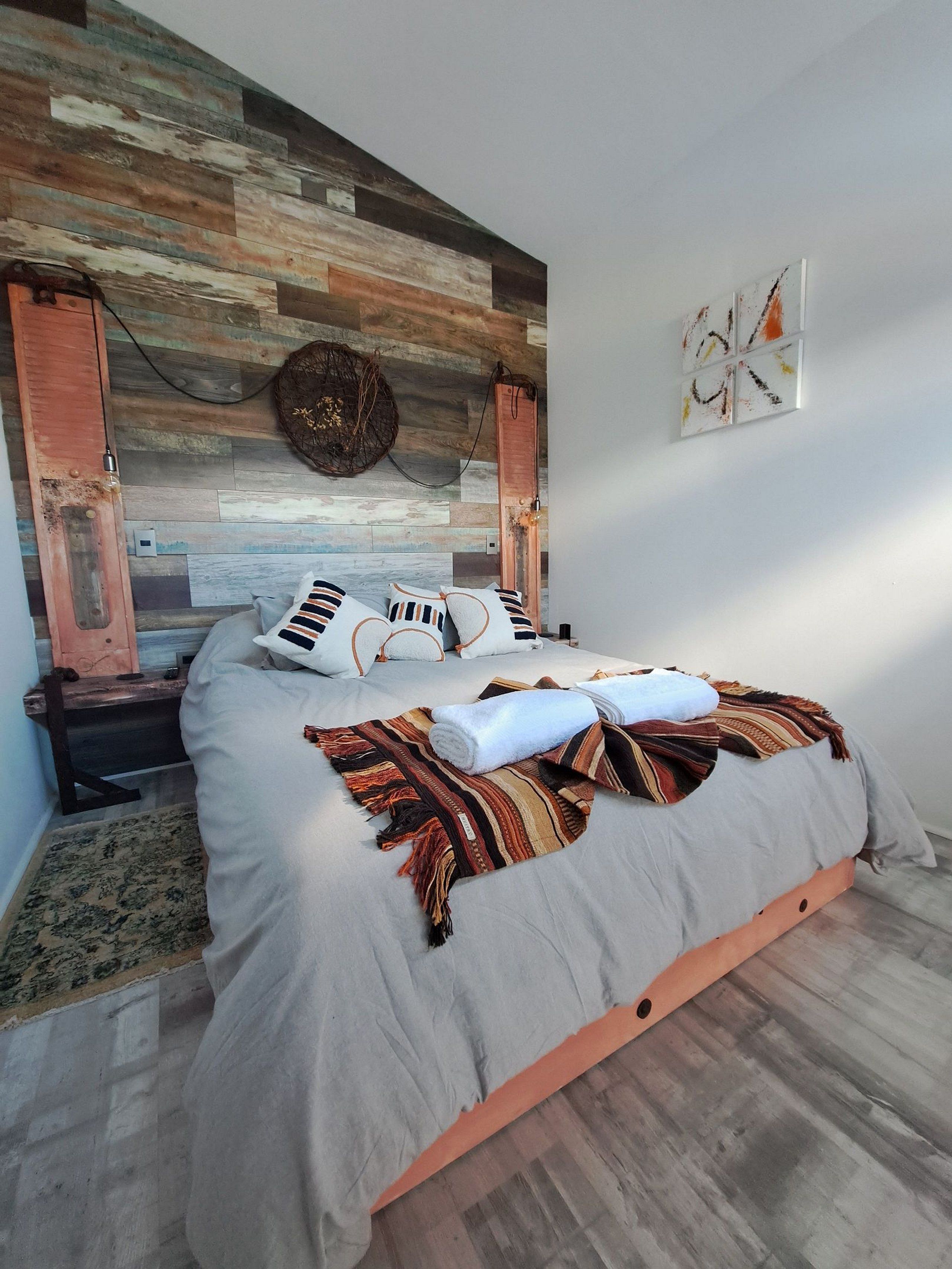 A modern bedroom with a wooden headboard, a bed with striped pillows, and a decorative wall piece.