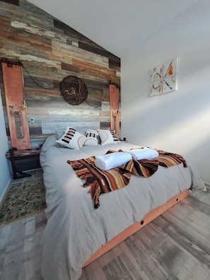 A modern bedroom with a wooden headboard, a bed with striped pillows, and a decorative wall piece. - Okeyloft 4 Coyhaique (Coyhaique)