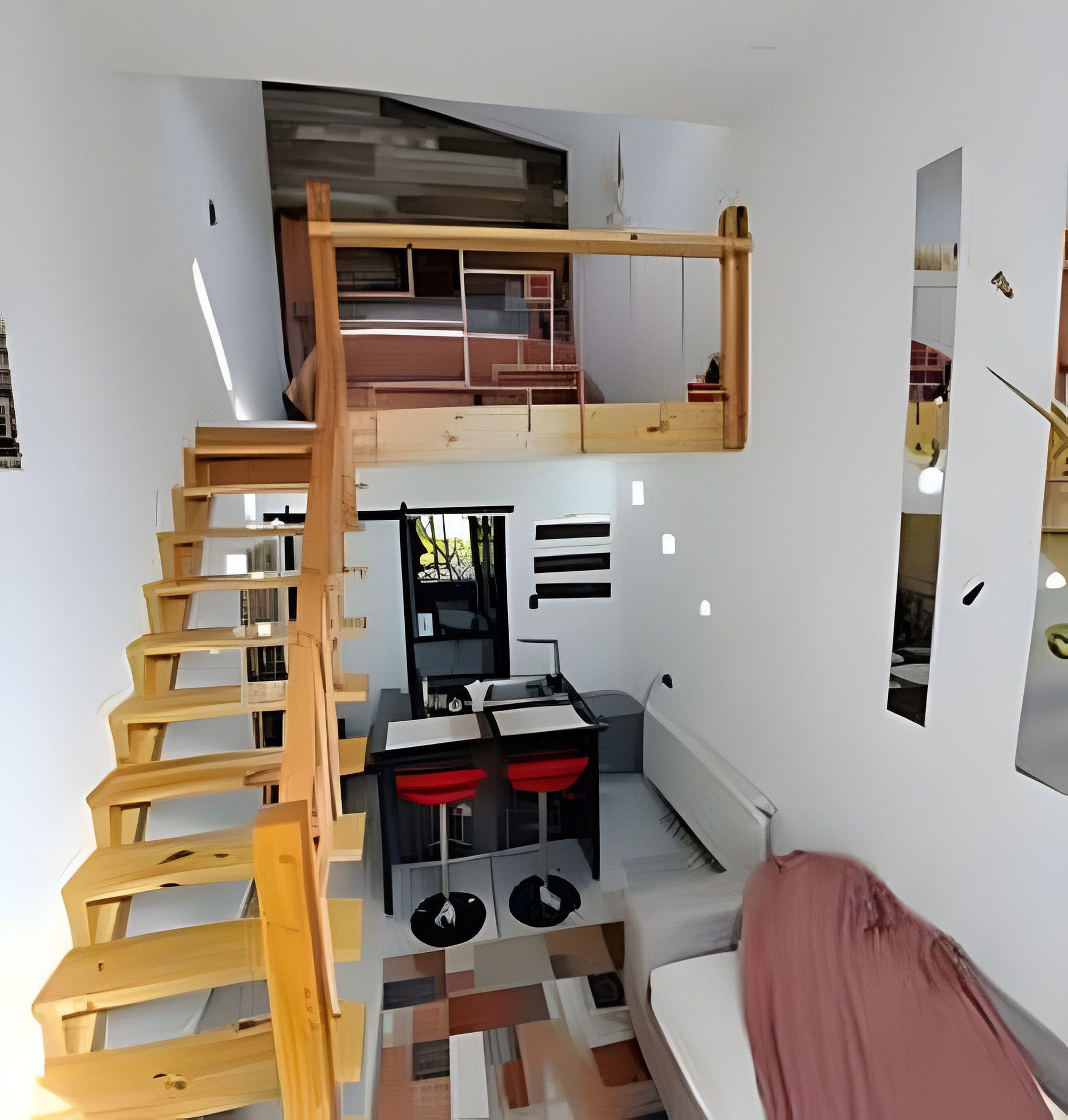 Quarto compacto com escada de madeira que dá acesso a um mezanino, uma cozinha compacta e uma área de estar com sofá.