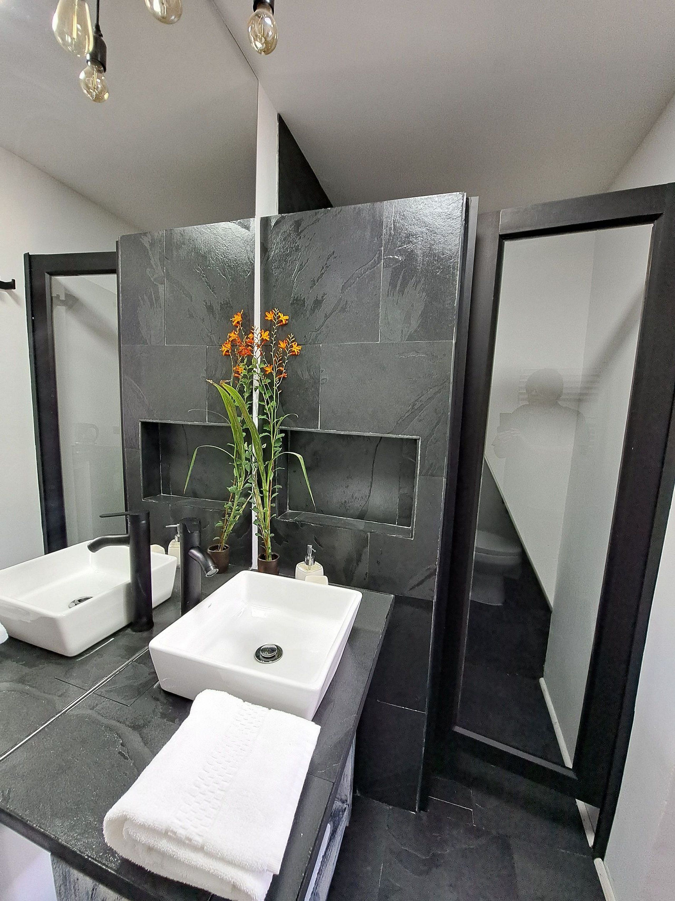 A modern bathroom with two sinks, a mirror, and a vase with flowers.