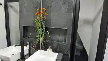 A modern bathroom with two sinks, a mirror, and a vase with flowers.