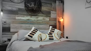 A bedroom with a bed, pillows, a wall with a textured design, and a wall-mounted light fixture.
