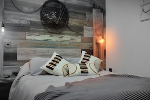 Un dormitorio con cama, almohadas, una pared con diseño texturizado y una lámpara de pared.