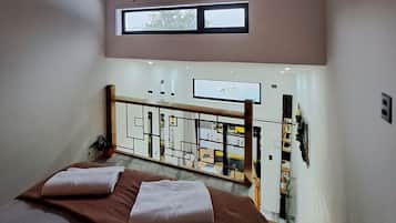 Un dormitorio con cama, televisor montado en la pared, ventana y vista del piso inferior.