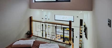 A bedroom with a bed, a TV mounted on the wall, a window, and a view of the room below.