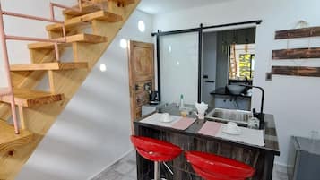 A modern kitchen with a wooden staircase, a central island with red bar stools, and a large mirror above the island.