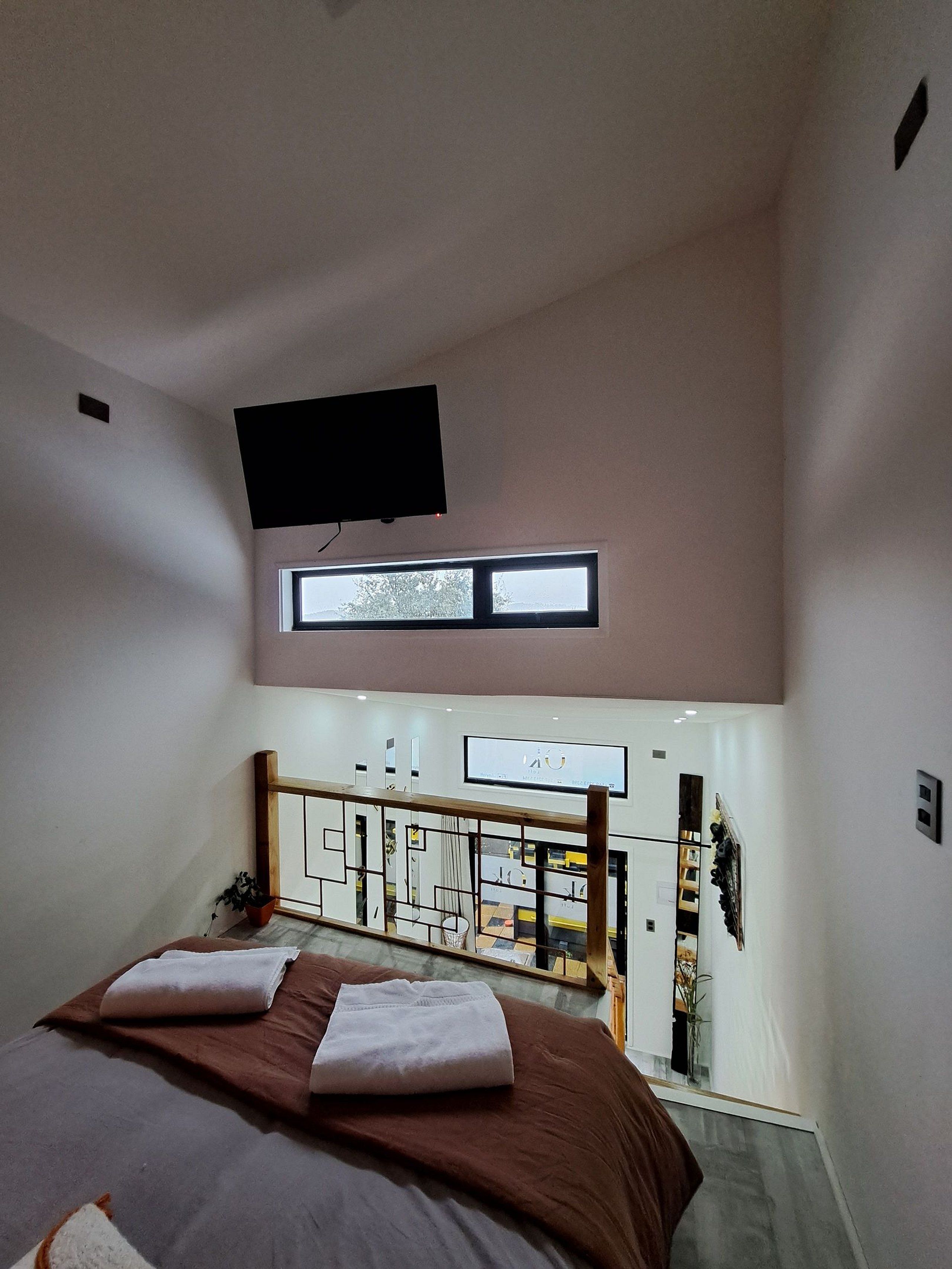 A bedroom with a bed, a TV mounted on the wall, a window, and a view of the room below.