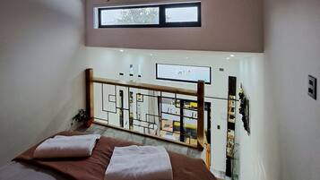 A bedroom with a bed, a TV mounted on the wall, a window, and a view of the room below.
