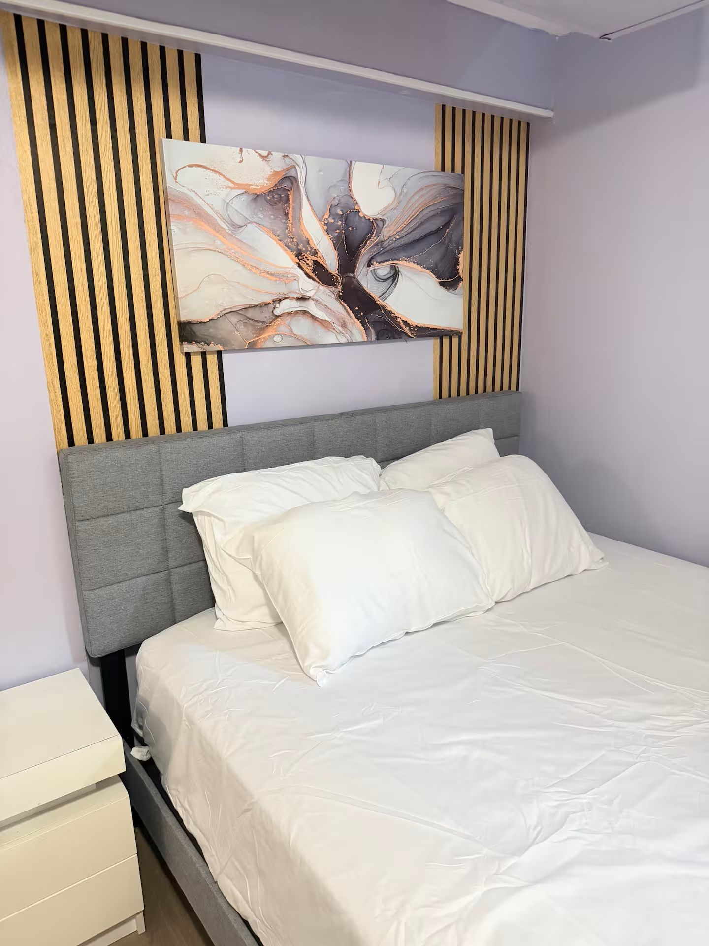 Un letto con una testiera grigia, biancheria da letto bianca e un grande quadro astratto sopra.