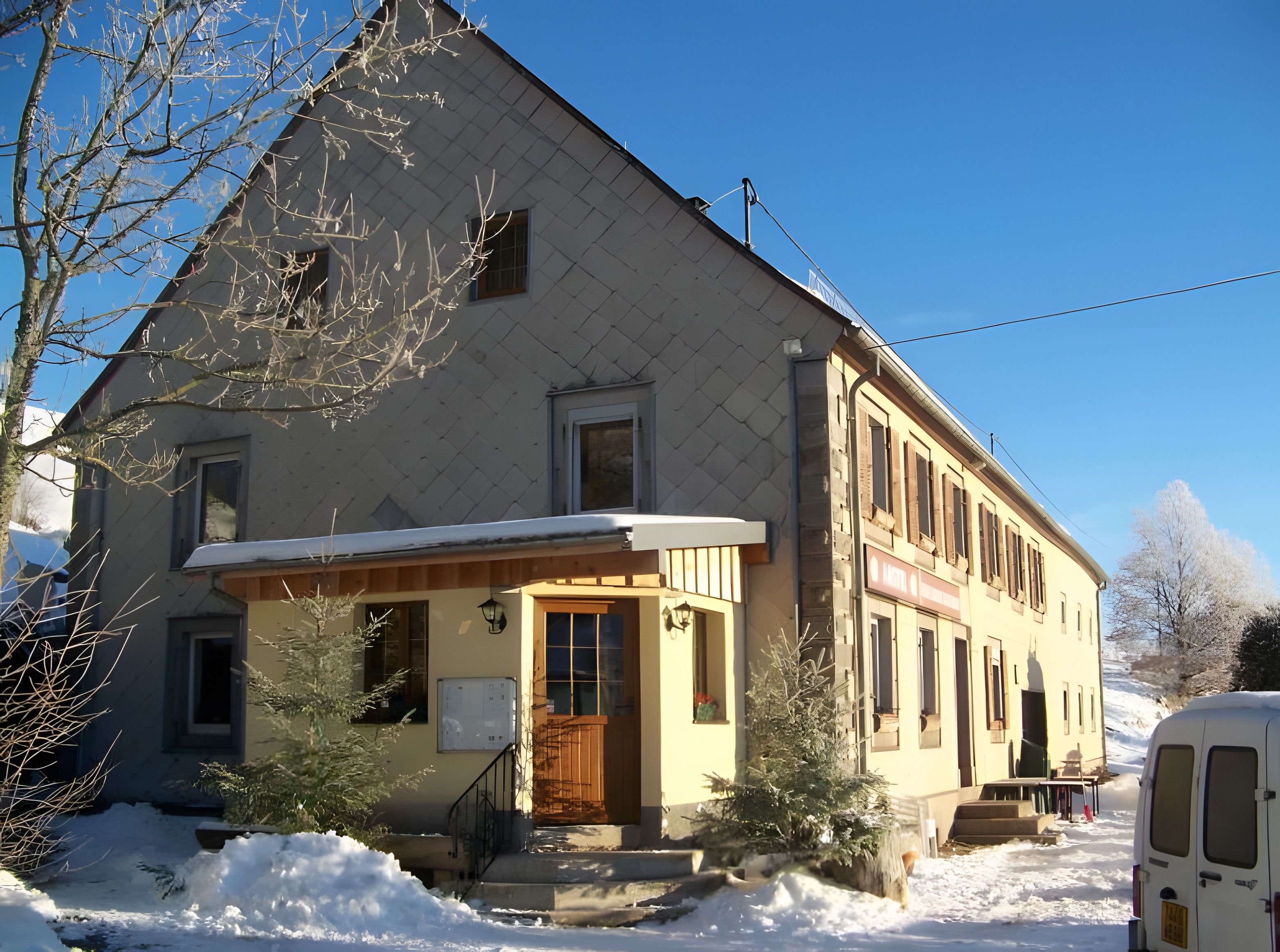 Un bâtiment à deux étages, avec un toit enneigé et un petit porche.