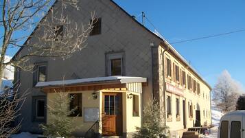 Un bâtiment à deux étages, avec un toit enneigé et un petit porche.