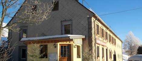 Un bâtiment à deux étages, avec un toit enneigé et un petit porche.