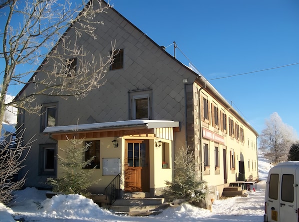 Un bâtiment à deux étages, avec un toit enneigé et un petit porche.