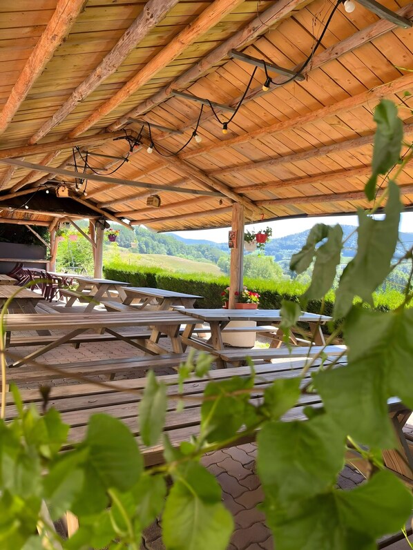 An outdoor wooden pavilion with picnic tables and hanging lights. - Guest Room "Chambre Sophie" with Mountain View and Shared Terrace (Orbey)