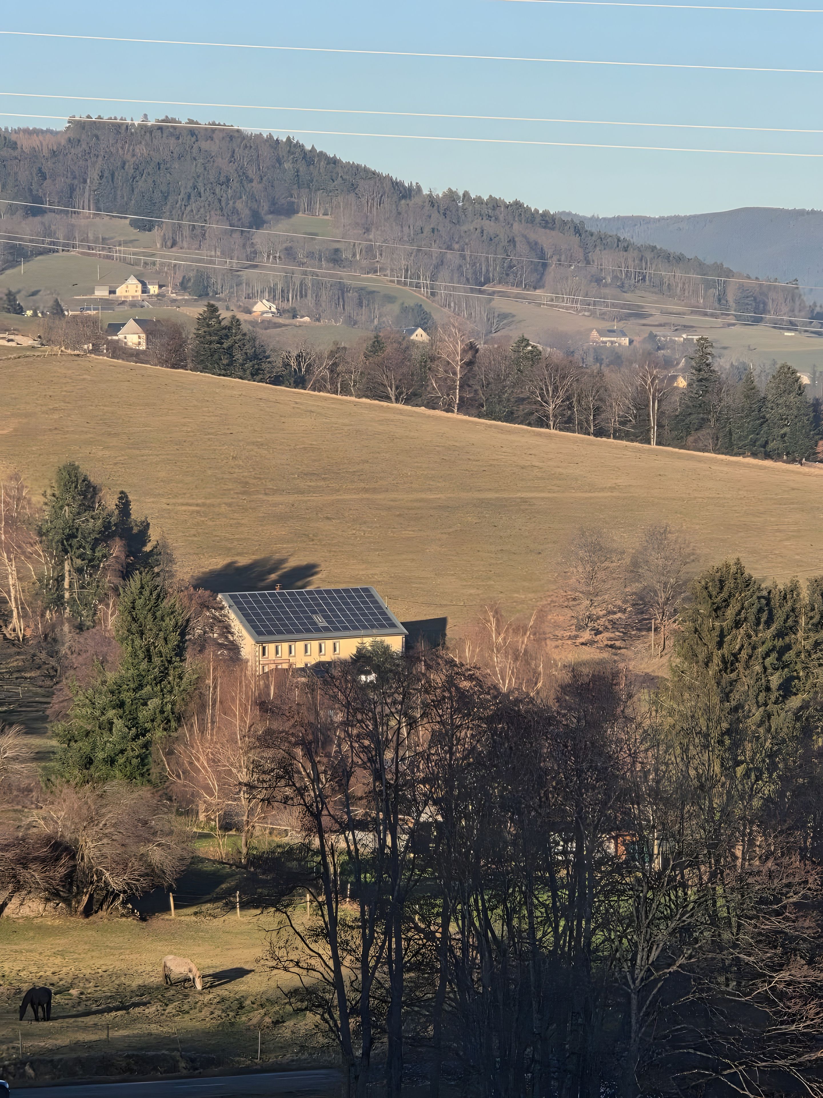 Un paysage rural avec un bâtiment doté de panneaux solaires, entouré d’arbres et de champs ouverts.