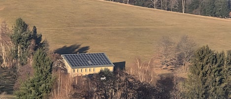 Un paysage rural avec un bâtiment doté de panneaux solaires, entouré d’arbres et de champs ouverts.