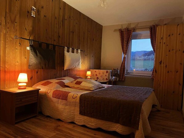 A room with a bed, two bedside tables, a window with curtains, and wooden walls. - Bed and Breakfast 'Chambre Noëlle' with Mountain View and Shared Terrace (Orbey)